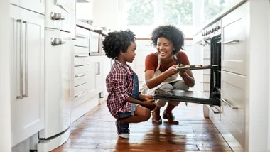 Woman and child baking together, smiling in a bright kitchen.