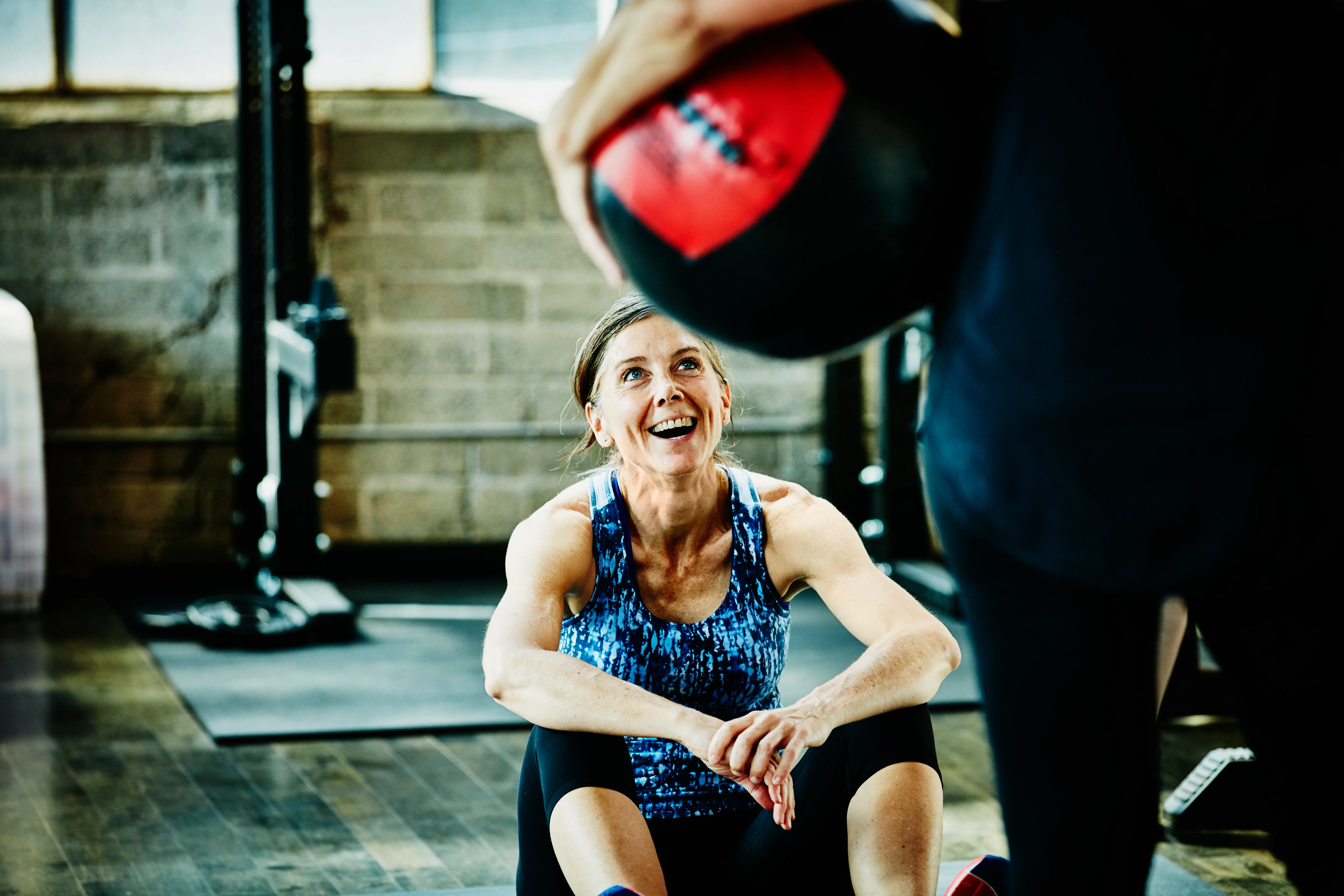 Laughing mature woman doing medicine ball crunches with partner during fitness class in studio