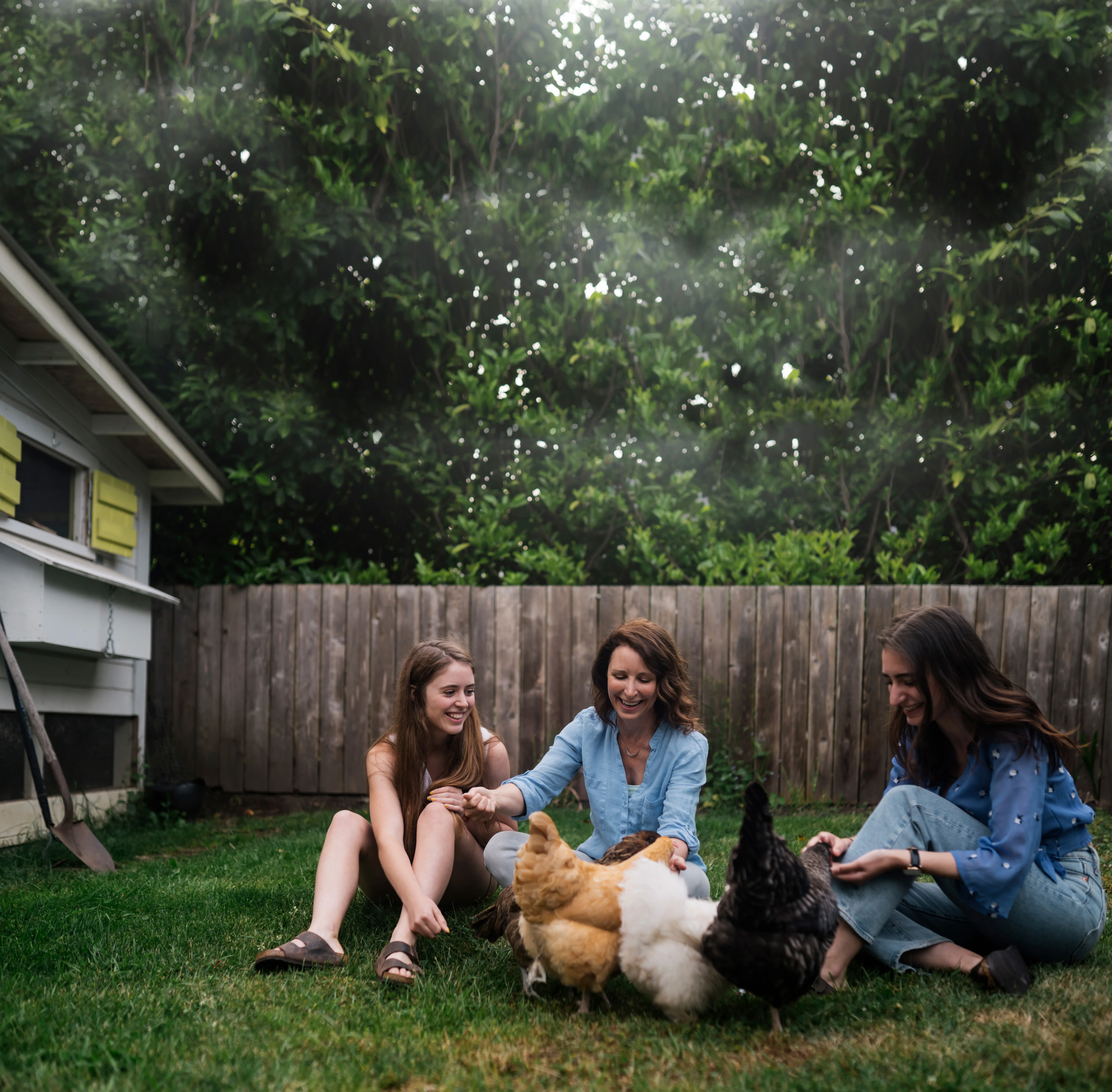 woman and two teenage girls feeding chickens