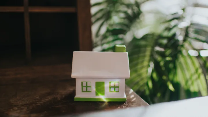 A toy house on a table with plants in the background to represent a first home