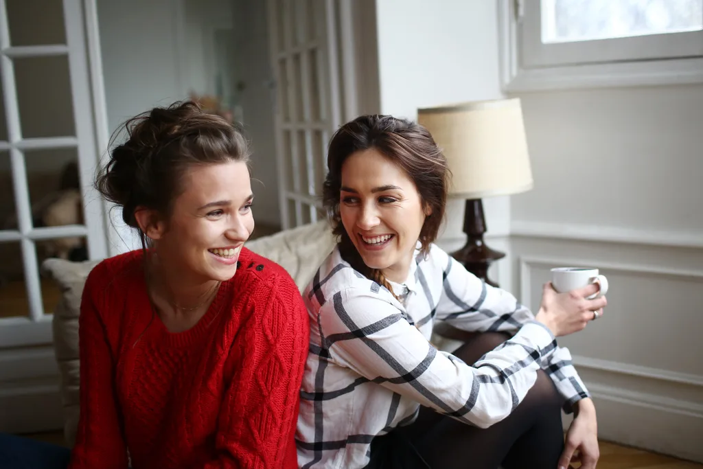 two women smiling at each other,one is drinking coffee.