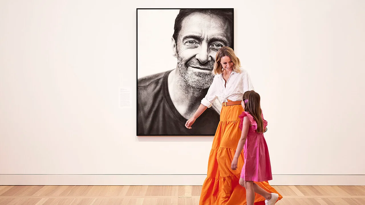A mother and daughter walk past a painting of Hugh Jackman in the National Portrait Gallery.