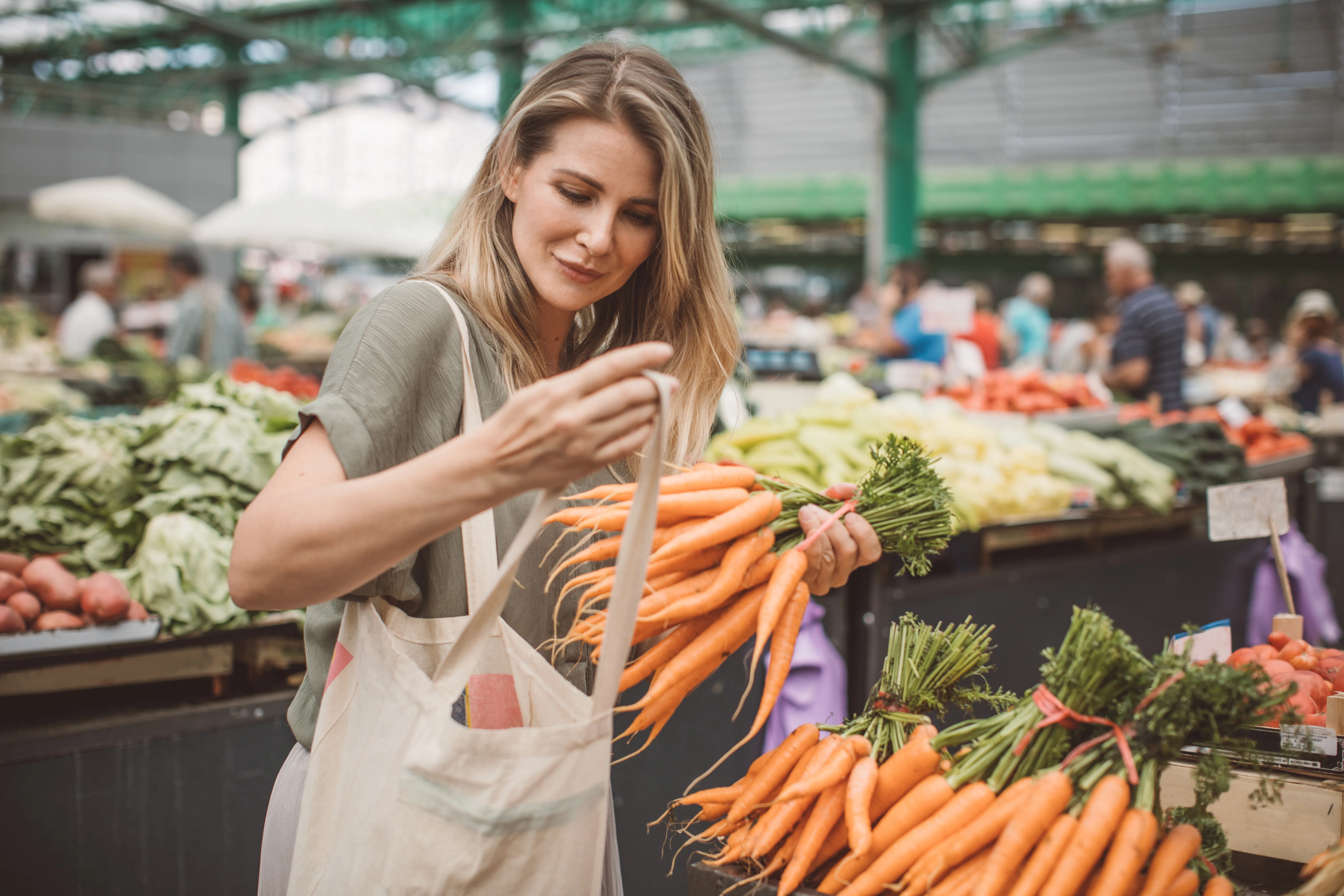 Cheerful woman selecting fresh vegetables in market, everything is fresh and organic.