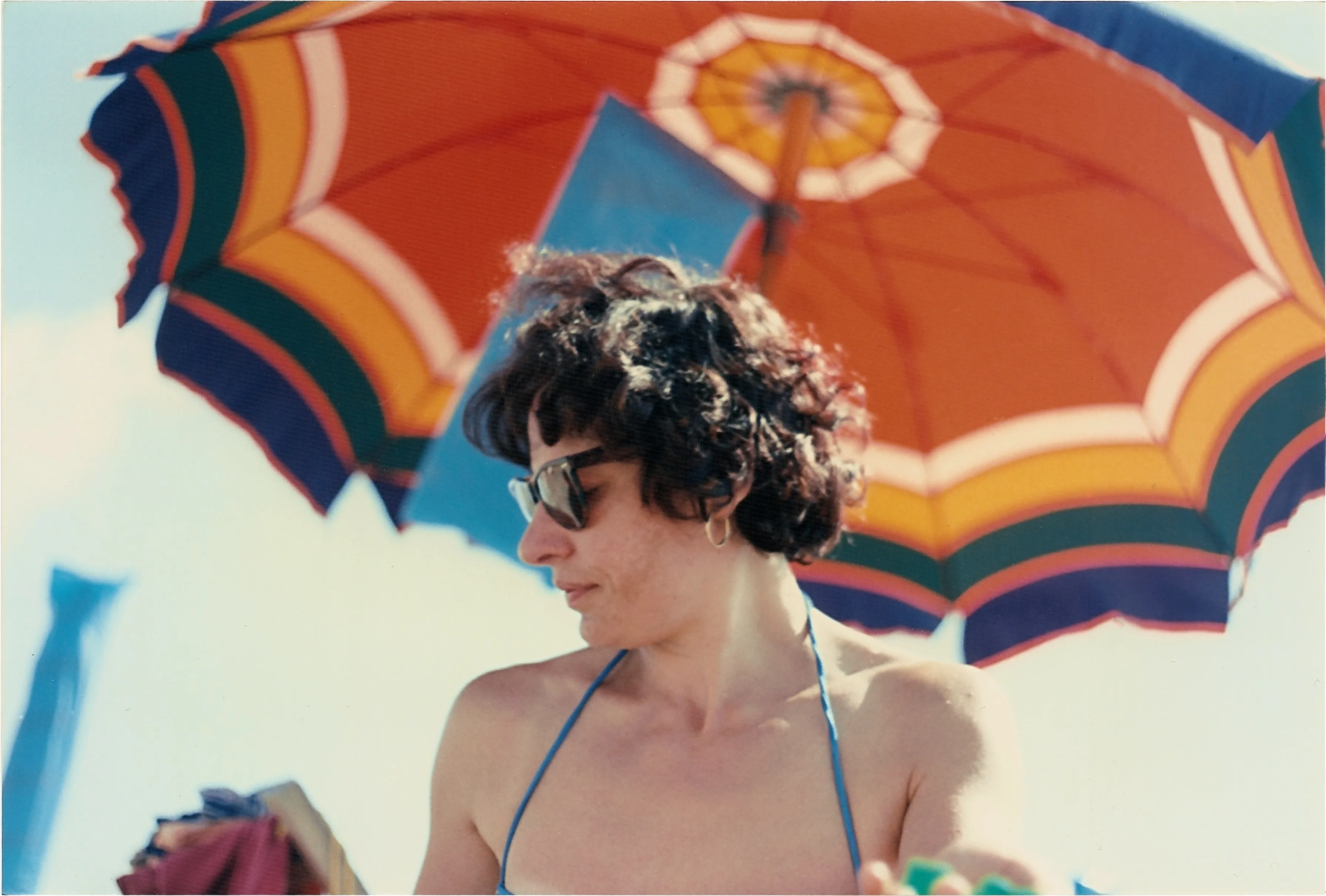 Analog picture of woman at beach with colorful umbrella on background.