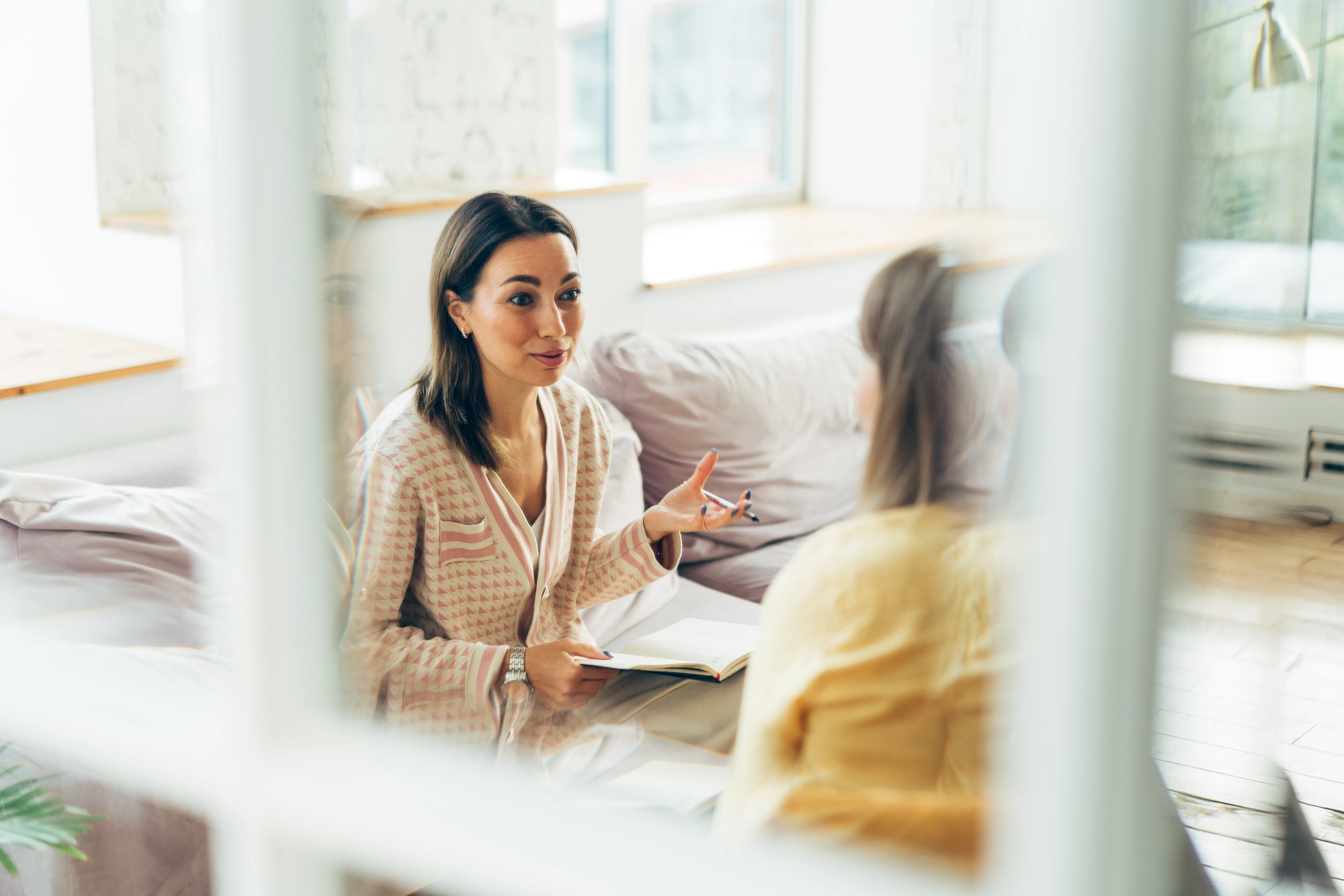 Two women sitting in armchairs and talking. Woman psychologist talking to patient woman. Coach giving hands to writing woman. Therapist's gestures. Female talking in coworking office