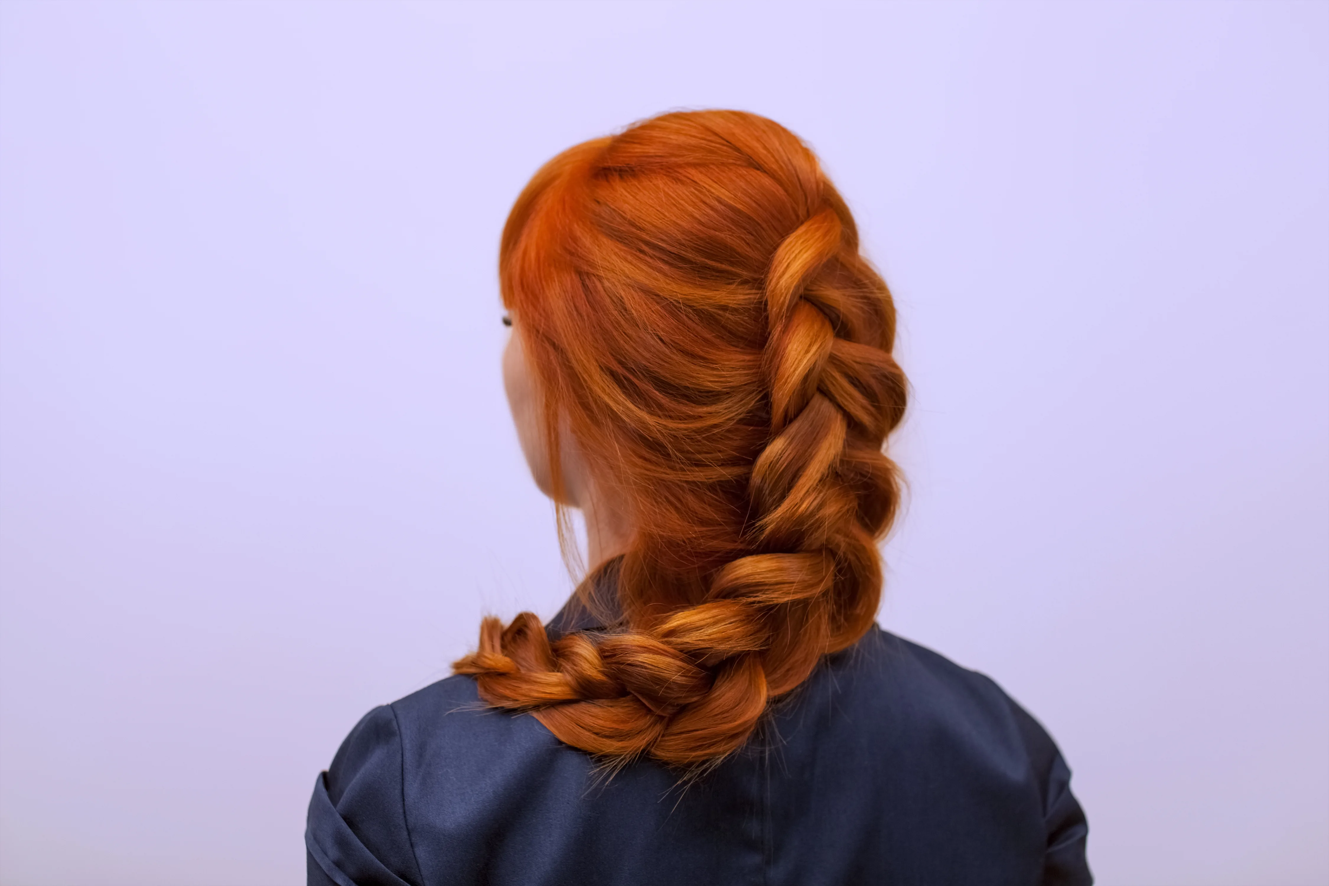 Beautiful girl with long red hair, braided with a French braid, in a beauty salon. Professional hair care and creating hairstyles.