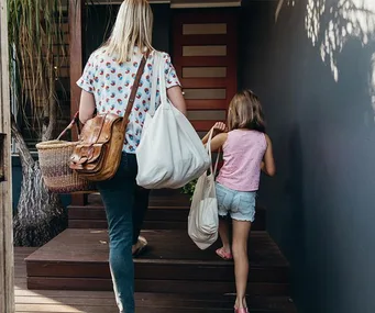 Woman and child carrying bags, entering a house together.