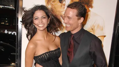 A smiling couple at a movie premiere event, with a poster in the background.