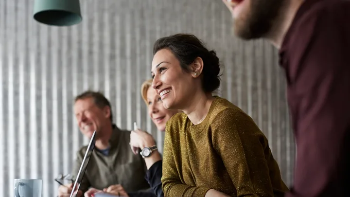 Group of four people smiling and sitting at a table during a meeting.