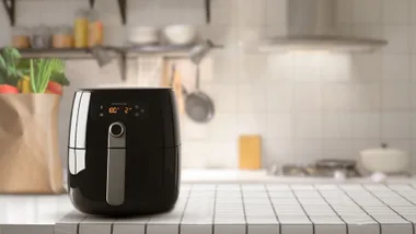 A black air fryer on a kitchen countertop with a blurred background and grocery bag nearby.