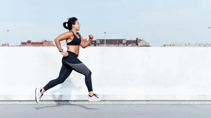 Woman in athletic gear running outdoors on a clear day.