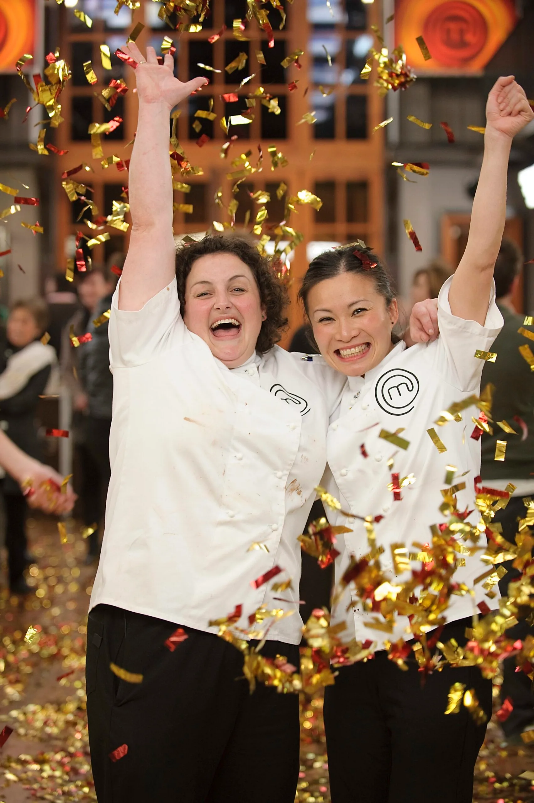 Two chefs in white jackets celebrate with confetti falling around them on a TV show set.