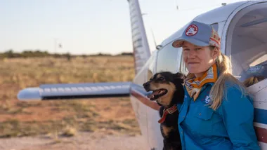 Woman with dog by a small plane.