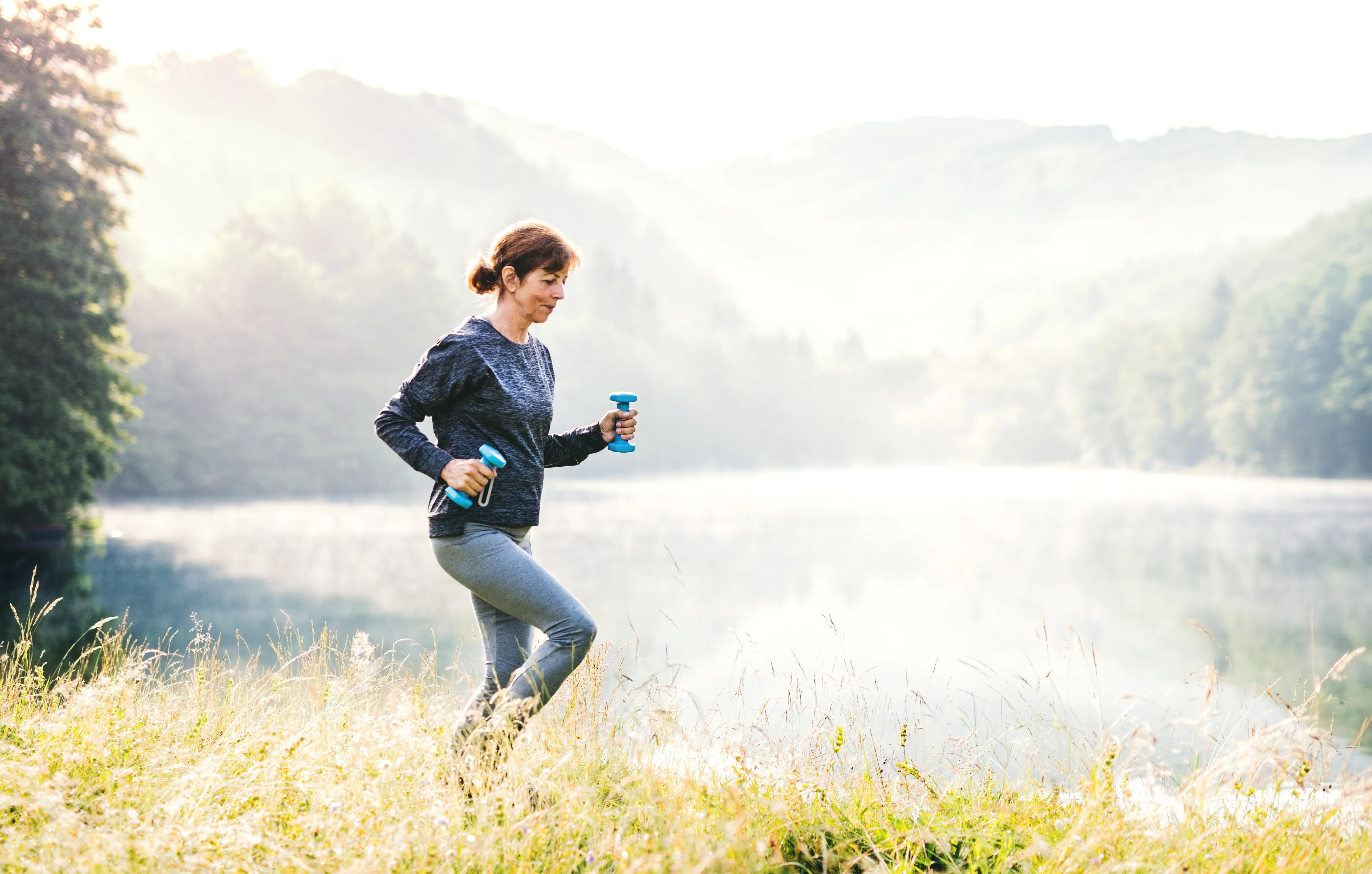An old female sportsperson doing sport by the lake outside in the countryside. Copy space.