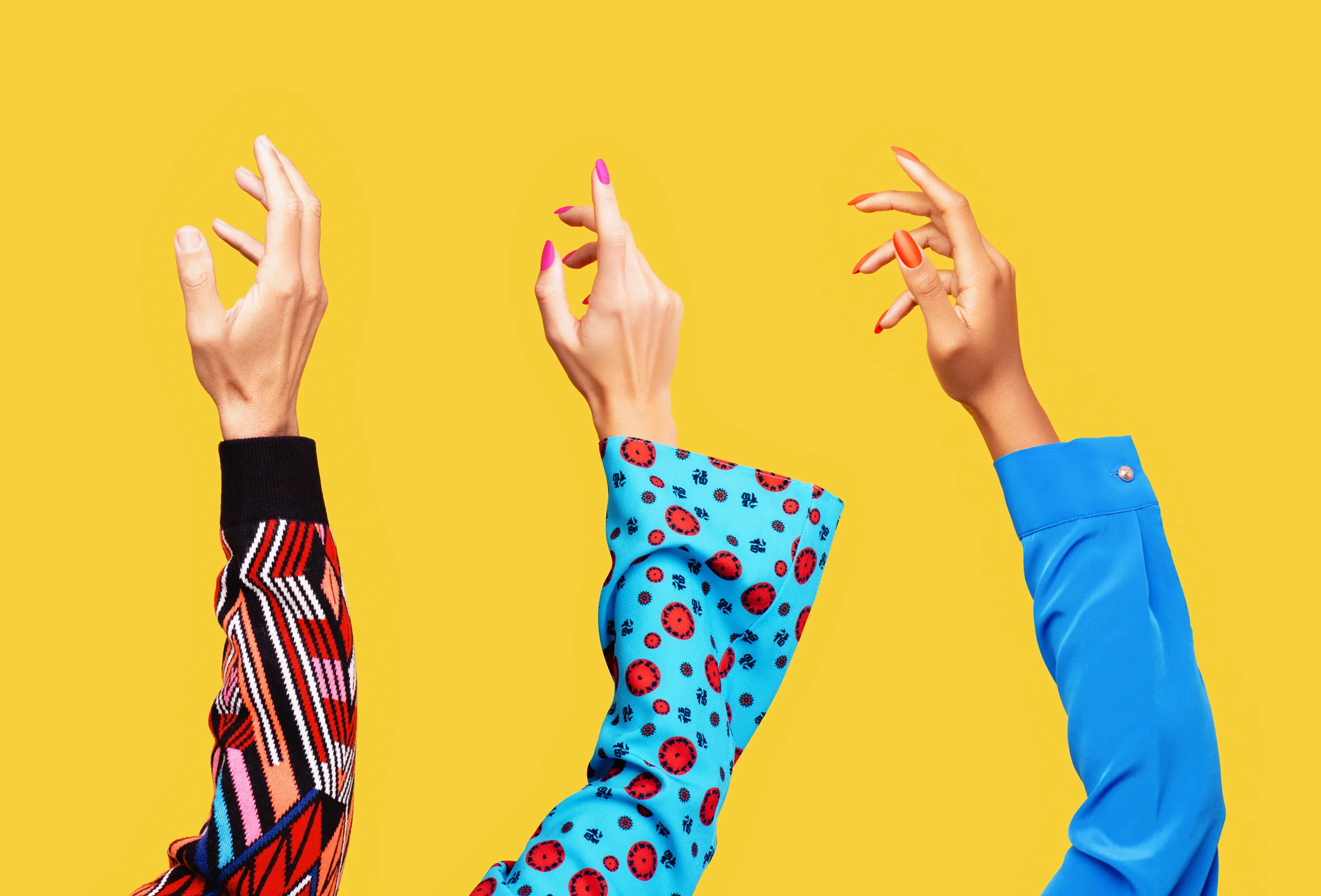 Hands of a white man, a white woman and a black woman reaching up into the air shot on yellow background.