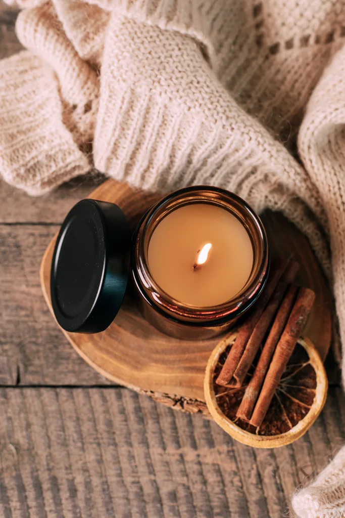 Candle in small amber glass jar with wooden wick on wooden stand on background. Copy space