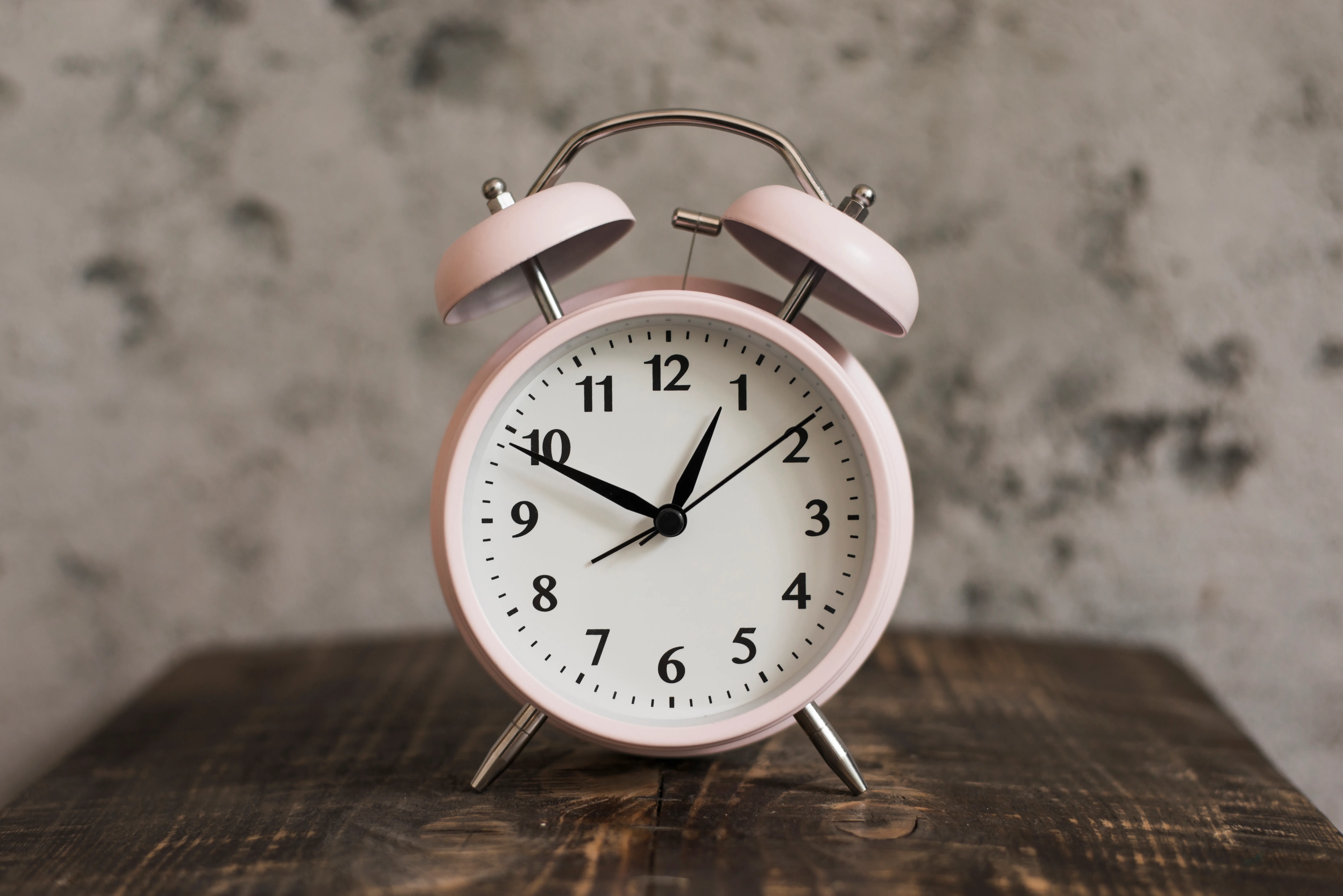 pink alarm clock wooden desk against weathered wall to represent sleep interruption.
