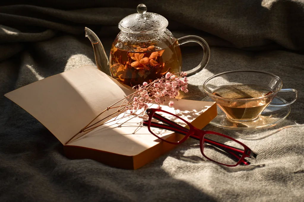 An opened book with a cup of tea on her side, reading a book on the bed.