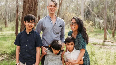 Family of five smiling in a forest, with trees in the background.