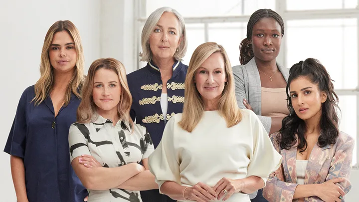 A group of six diverse women stand confidently in business attire against a light background.