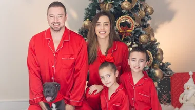 Family in red pajamas with a dog in front of a Christmas tree decorated with golden ornaments.