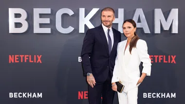 "Two people pose at the premiere of Netflix's 'Beckham' in front of a backdrop with large letters and logos."