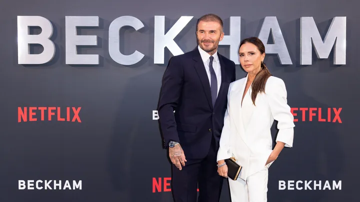 "Two people pose at the premiere of Netflix's 'Beckham' in front of a backdrop with large letters and logos."