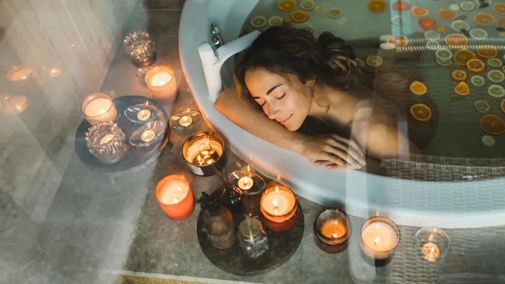 Woman relaxing in a candle-lit bathtub with floating citrus slices, eyes closed, serene atmosphere.