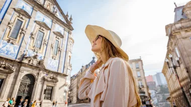 Woman in a sunhat smiling while sightseeing near a historic, azulejo-tiled building in a European city.