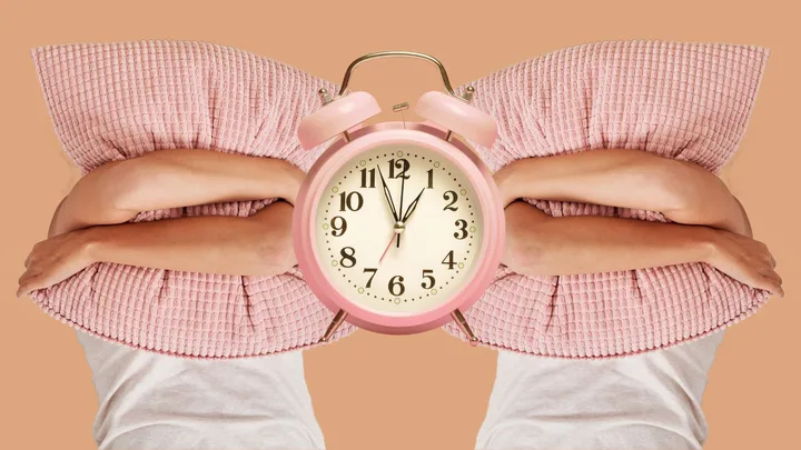 Person hugging pink pillow with alarm clock in center, on a beige background.