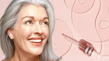 Smiling woman with gray hair next to dropper on a soft pink background.