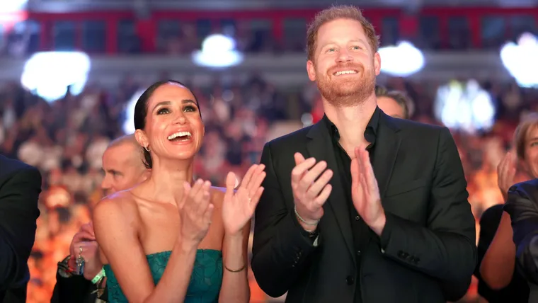 A smiling couple clapping at an event with a blurred audience in the background.