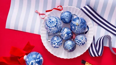 Blue and white patterned Christmas ornaments on a white plate, with striped ribbon on a red and striped background.