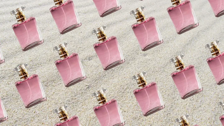 Pink perfume bottles arranged on a sandy background, creating a repeating pattern.