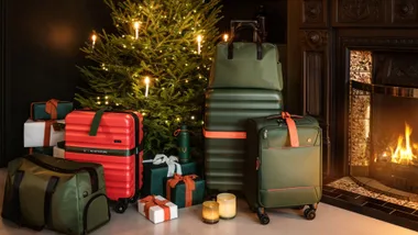 Luggage and gifts by a Christmas tree and fireplace, featuring Antler bags in festive setting.