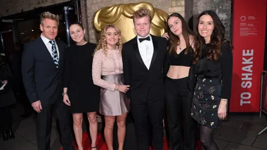 A group of people dressed formally, standing on a red carpet in front of a golden backdrop.