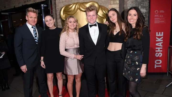A group of people dressed formally, standing on a red carpet in front of a golden backdrop.