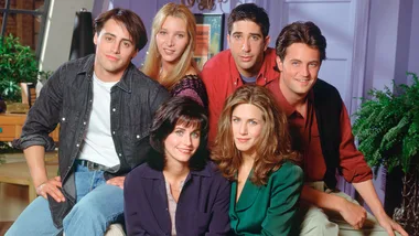Cast of "Friends" smiling in a living room setting.