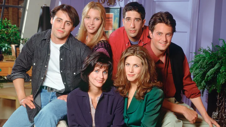 Cast of "Friends" smiling in a living room setting.