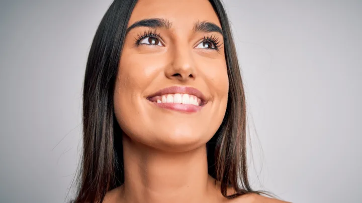 Smiling woman with long dark hair looking upwards against a plain background.