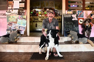 Man with a dog sitting in front of a rustic cafe, surrounded by local decor and a menu board.