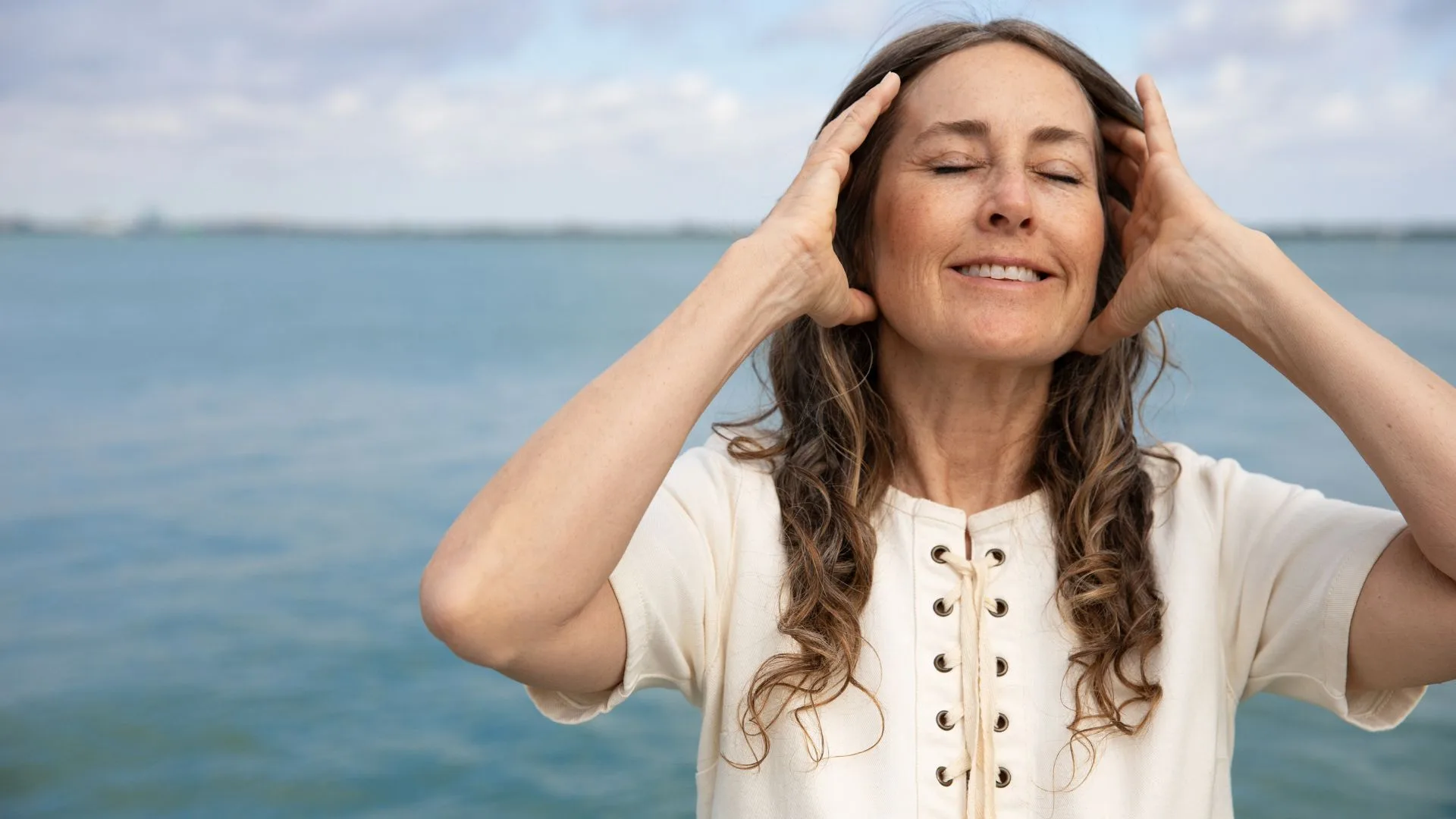 Woman with eyes closed smiling holding her hands up to her temples