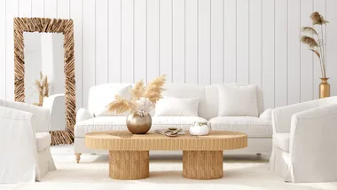 Modern living room with white sofa, textured wooden mirror, and round coffee table decorated with pampas grass.