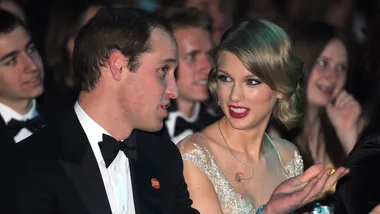 Two elegantly dressed people seated at an event, engaged in conversation.