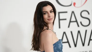 A woman in a blue dress at a fashion event, smiling over her shoulder.