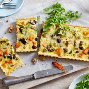 Vegetable tart slices with olives and rocket on parchment, served with a knife.