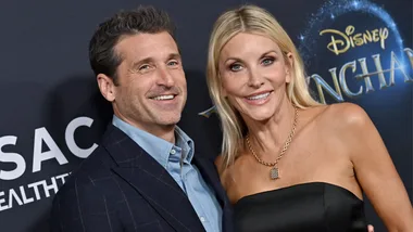 Smiling man and woman pose at the "Disenchanted" premiere with Disney logo in background.