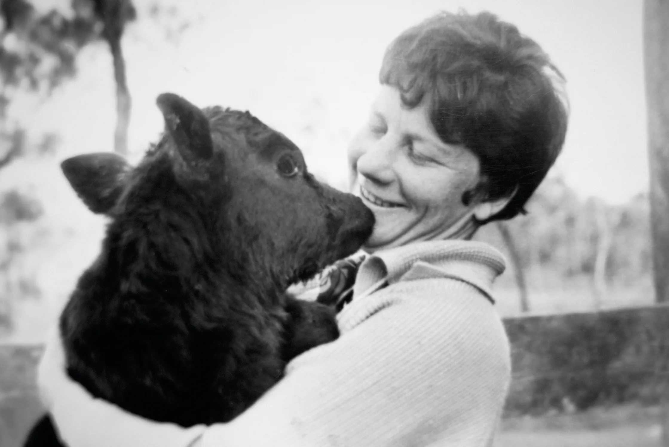 Black and white photo of Girlie as a young woman holding a calf and smiling.