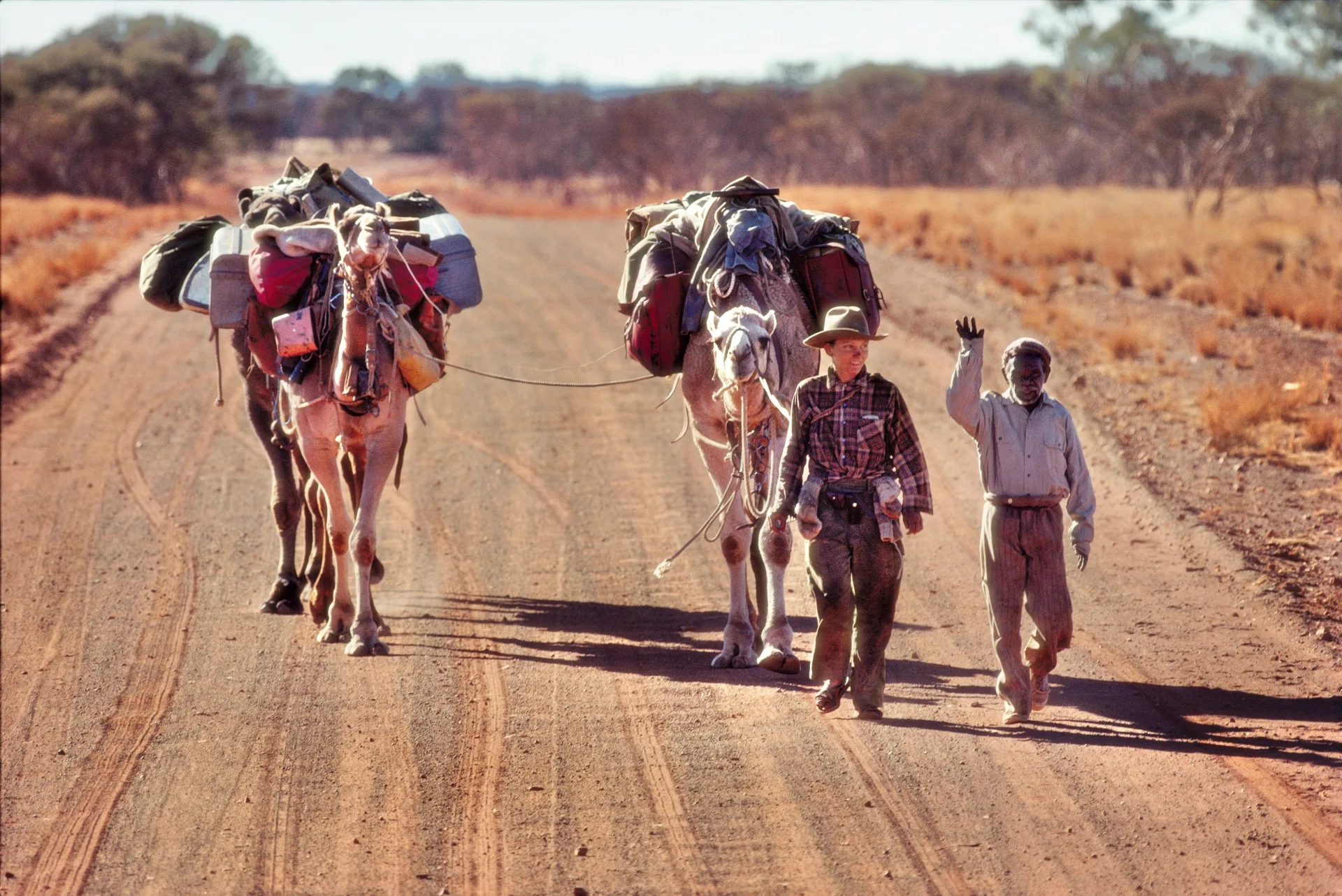 Robyn Davidson with two camels and a person on a dirt track