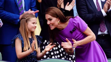 A woman in a purple dress and a young girl in a polka dot dress clapping and smiling at an event.